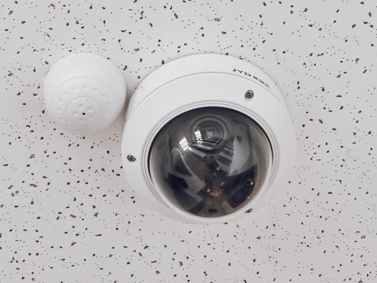 about-02 Close-up of a round dome surveillance camera installed on a speckled ceiling for security monitoring.